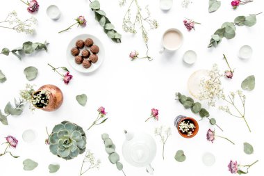 Gül tomurcuklu çalışma alanı, okaliptüs, sulu çay, bir fincan kakao, beyaz arka planda tatlılar. Düz konum, genel manzara, ev ofis çalışma alanı