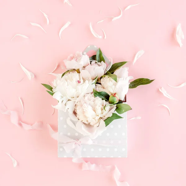 Bouquet beige di peonie in una busta per fiori su sfondo rosa. Biglietto di auguri minimale concetto floreale. Posa piatta, vista dall'alto. — Foto Stock