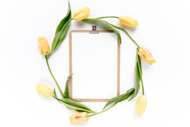 Pano beyaz arka planda izole edilmiş güzel sarı lalelerle süsleniyor. Düz yerde, üst tarafta. Minimalist ofis masası. Güzellik günlüğü konsepti.