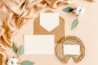 Sahte düğün davetiyesi, boş tebrik kartı ve el işi zarfı, yeşil yapraklı okaliptüs. Düz yatış, üst görünüm.