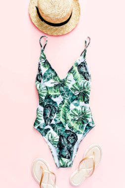 Kadın plaj aksesuarları: tropik baskılı mayo, pembe arka planda hasır şapka. Yaz dönemi. Düz yatıyordu