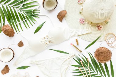 Kadınsı bej mayo plaj aksesuarları, tropik palmiye yaprağı dalları, beyaz arka planda hindistan cevizleri. Yaz dönemi. Yol çerçevesi ayarlandı. 