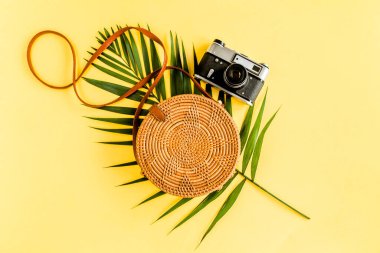 Sarı arka planda gezgin aksesuarları konsepti. Moda el yapımı doğal turuncu çanta, retro kamera ve tropik yapraklar.. 