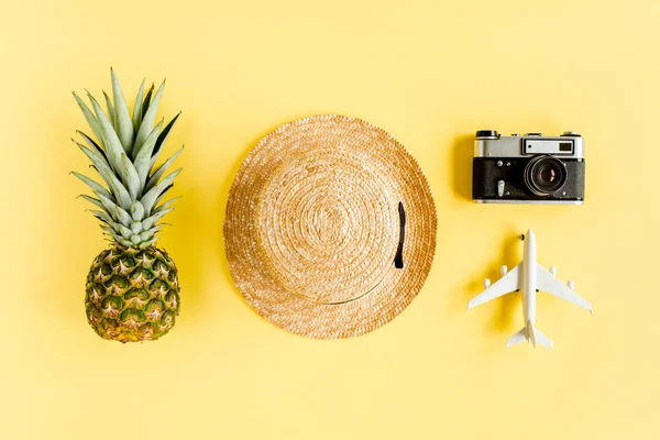 Traveler accessori concetto su sfondo giallo. Fotocamera retrò, modellino aereo, aeroplano, cappello di paglia e ananas. — Foto Stock