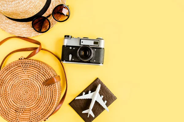 Eco saco de vime, câmera retro, avião modelo, avião e chapéu de palha. Conceito de acessórios para viajantes em fundo amarelo. — Fotografia de Stock