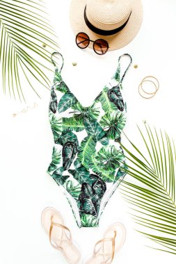 Kadın plaj aksesuarları: tropikal desenli mayo, beyaz arka planda hasır şapka. Yaz arkaplanı. 