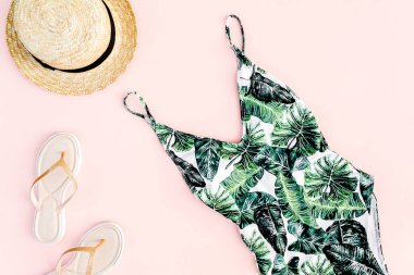 Kadın plaj aksesuarları: tropik baskılı mayo, pembe arka planda hasır şapka. Yaz dönemi. Düz yatıyordu