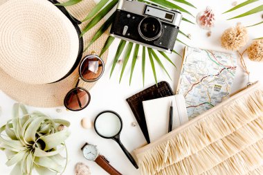 Retro kamera, hasır şapka, çanta, güneş gözlüğü, harita ve tropikal palmiye yaprağıyla beyaz arka planda gezgin aksesuarları.