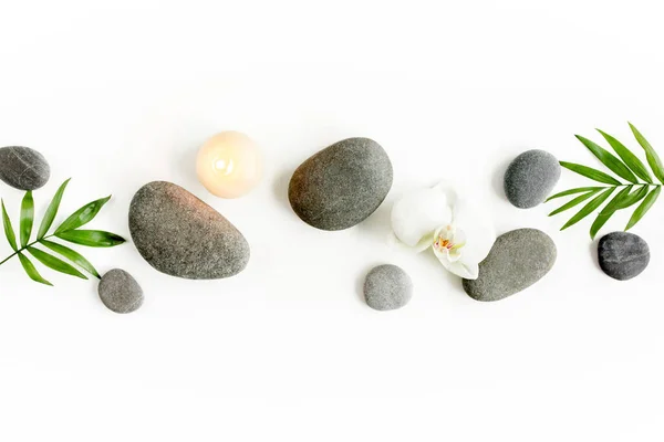 Wellness-Steine, Palmblätter, blumenweiße Orchidee, Kerze und Zen wie graue Steine auf weißem Hintergrund. Flache Lage, Draufsicht — Stockfoto