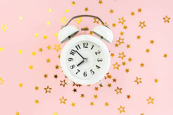 Alarm clock covered golden stars confetti, decoration on a pink, festive background. Christmas or New Year pattern. Colorful celebration, birthday. — Stock Photo, Image