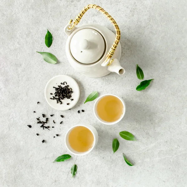 Herbal tea with two white tea cups and teapot, with green tea leaves. Flat lay, top view. Tea concept