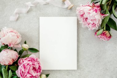 Sahte davetiye, boş kağıt tebrik kartı ve gri taş masadaki şakayıklar. Çiçek arkaplanı. Düz yatış, üst görünüm.