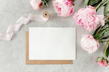 Sahte davetiye, boş kağıt tebrik kartı ve gri taş masadaki şakayıklar. Çiçek arkaplanı. Düz yatış, üst görünüm.