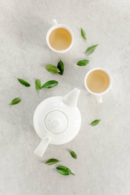 İki beyaz çay fincanı ve yeşil çay yapraklı çaydanlık ile bitki çayı. Düz yerde, üst tarafta. Çay konsepti