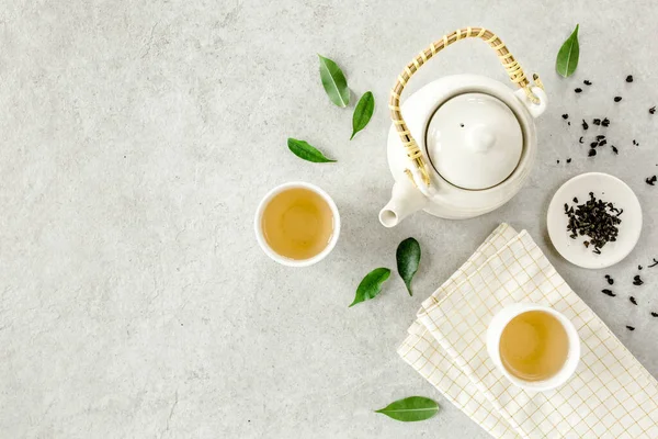 İki beyaz çay fincanı ve yeşil çay yapraklı çaydanlık ile bitki çayı. Düz yerde, üst tarafta. Çay konsepti