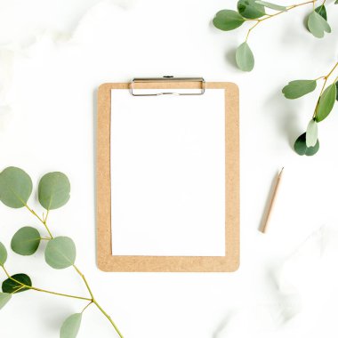 Beyaz arka planda pano ve yaprak okaliptüslü çalışma alanı. Ev ofis masasının düz yatağı, üst görünüm. 