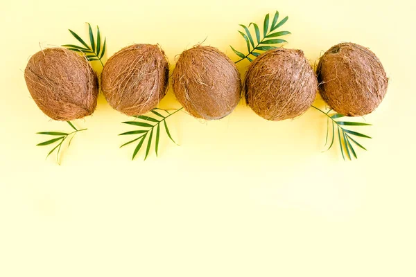 Modello con noci di cocco e foglie di palma tropicale su sfondo giallo. Sfondo tropicale astratto. Posa piatta, vista dall'alto. — Foto Stock