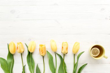 Sarı laleler, beyaz, ahşap arka planda izole edilmiş bir fincan çay. Düz uzan, üst görünüm