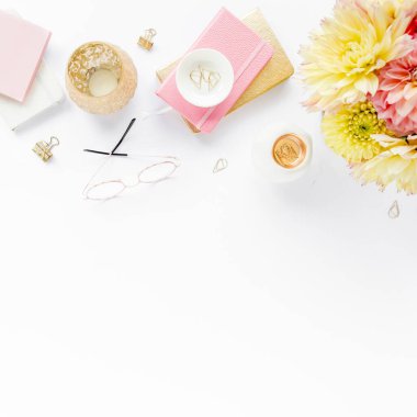 Ev ofisinin masası düzdü. Pembe ve bej gülleri, çiçekleri, aksesuarları, altın ve pembe günlüğü, beyaz ahşap arka planı olan kadın çalışma alanı. Üst görünüm 