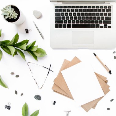 Ofis masası çalışma alanı boş, yeşil yapraklı. Dizüstü bilgisayar, beyaz arka planda gözlük. Dergiler, web siteleri, sosyal medya. Düz yatış, üst görünüm.