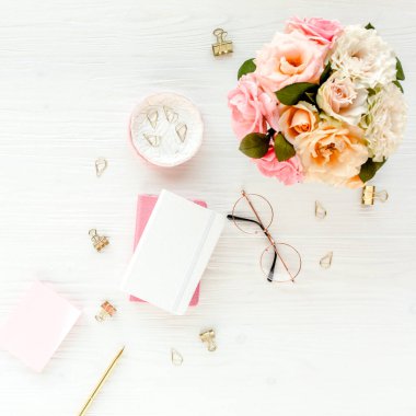 Düz uzanmış kadınların ofis masası. Pembe güller, çiçek buketi, aksesuarlar, altın günlük, beyaz ahşap arka planda gözlük.