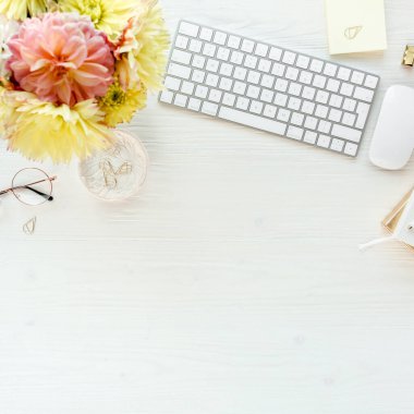 Düz uzanmış kadınların ofis masası. Bilgisayarlı kadın çalışma alanı, pembe ve sarı güller çiçekler, aksesuarlar, günlük, beyaz arka planda gözlük. Üst görünüm