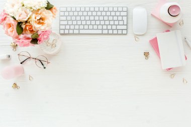 Düz uzanmış kadınların ofis masası. Bilgisayarlı kadın çalışma alanı, pembe güller çiçekler, aksesuarlar, altın günlük, beyaz arka planda gözlük. Üst görünüm 
