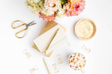 Ev ofisinin masası düzdü. Pembe güllü kadın çalışma alanı, yıldız çiçeği buketi, altın aksesuarlar, beyaz arka planda günlük. Üst görünüm.