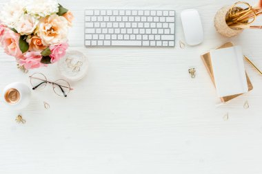 Düz uzanmış kadınların ofis masası. Bilgisayarlı kadın çalışma alanı, pembe güller çiçekler, aksesuarlar, altın günlük, beyaz arka planda gözlük. Üst görünüm 