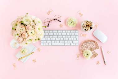 Tarz sahibi, pembe kadınların ofis masası. Bilgisayarlı çalışma alanı, buket ranunculus ve güller, pembe arka planda pano. Düz yatıyordu. Üst görünüm.