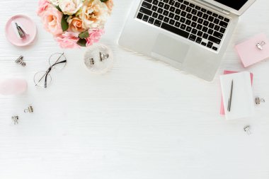 Düz uzanmış kadınların ofis masası. Dizüstü bilgisayarı, pembe gülleri, çiçekleri, aksesuarları, günlüğü, beyaz tahta arka planda gözlüğü olan kadın çalışma alanı. Üst görünüm.