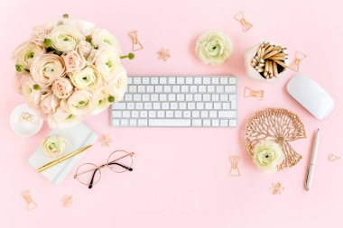 Tarz sahibi, pembe kadınların ofis masası. Bilgisayarlı çalışma alanı, buket ranunculus ve güller, pembe arka planda pano. Düz yatıyordu. Üst görünüm.