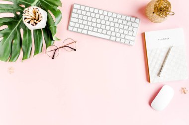 Ev ofisinin masası düzdü. Bilgisayarlı kadın çalışma alanı, tropikal palmiye yaprakları, pembe arka planda aksesuarlar. Üst görünüm arkaplanı. 
