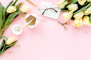 Lale çiçeği buketli, altın aksesuarlı, pembe arka planlı bir kadın çalışma alanı. Düz uzanmış kadınların ofis masası. Üst görünüm kadınsı arkaplan