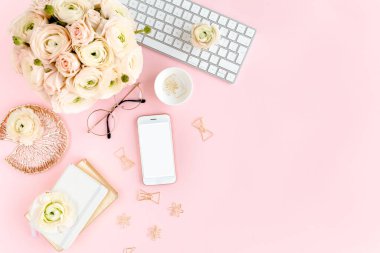 Tarz sahibi, pembe kadınların ofis masası. Bilgisayarlı çalışma alanı, buket ranunculus ve güller, pembe arka planda telefon. Düz yatıyordu. Üst görünüm.