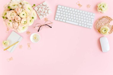Tarz sahibi, pembe kadınların ofis masası. Bilgisayarlı çalışma alanı, buket ranunculus ve güller, pembe arka planda pano. Düz yatıyordu. Üst görünüm.