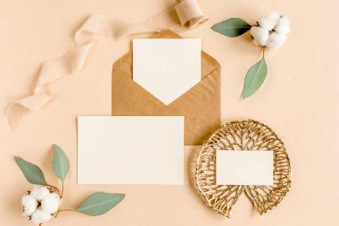 Sahte düğün davetiyesi, boş tebrik kartı ve el işi zarfı, yeşil yapraklı okaliptüs. Düz yatış, üst görünüm.