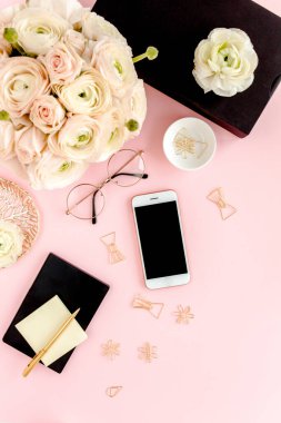 Tarz sahibi, pembe kadınların ofis masası. Bilgisayarlı çalışma alanı, buket ranunculus ve güller, pembe arka planda telefon. Düz yatıyordu. Üst görünüm.