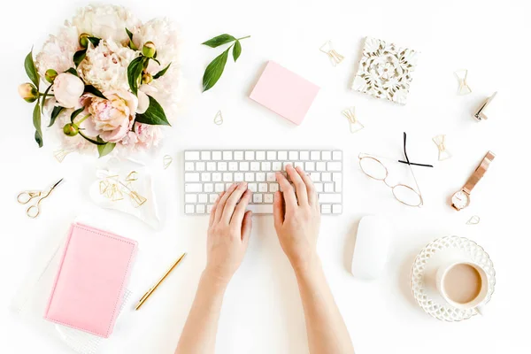 Escritorio de oficina de mujeres laicas planas. Espacio de trabajo femenino con manos femeninas, ordenador, ramo de peonías rosadas, accesorios sobre fondo blanco. Vista superior. —  Fotos de Stock