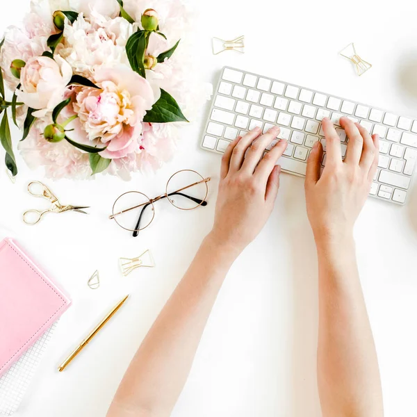 Escritorio de oficina de mujeres laicas planas. Espacio de trabajo femenino con manos femeninas, ordenador, ramo de peonías rosadas, accesorios sobre fondo blanco. Vista superior. —  Fotos de Stock