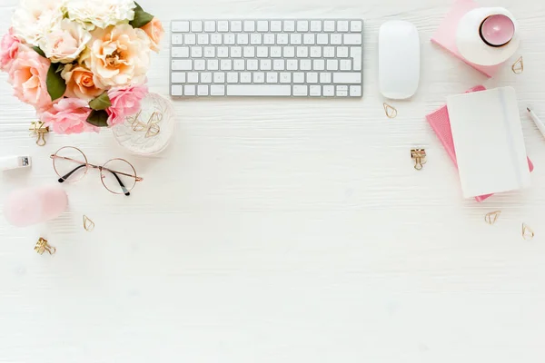 Flat lay womens office desk. Female workspace with computer, pink roses flowers, accessories, golden diary, glasses on white background. Top view