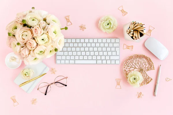 Stylized, pink womens home office desk. Workspace with computer, bouquet ranunculus and roses, clipboard on pink background. Flat lay. Top view.