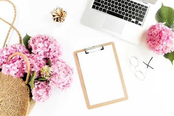 Meja wanita yang bergaya. Ruang kerja dengan papan klip, laptop, bouquet hydrangea, aksesoris pada latar belakang putih. Berbaringlah. Tampilan atas. — Stok Foto