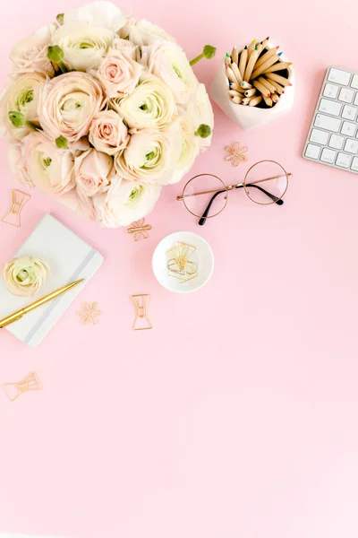 Stylized, pink womens home office desk. Workspace with bouquet ranunculus and roses, clipboard on pink background. Flat lay. Top view.