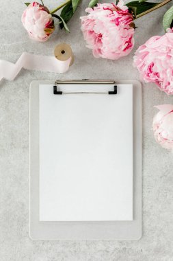 Sahte davetiye, boş kağıt tebrik kartı ve gri taş masadaki şakayıklar. Çiçek arkaplanı. Düz yatış, üst görünüm.