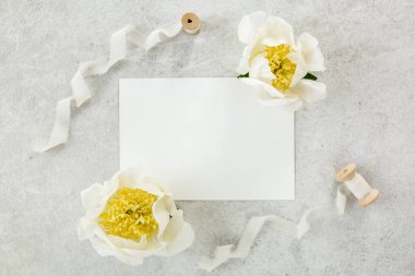 Sahte davetiye, boş kağıt tebrik kartı ve gri taş masadaki şakayıklar. Çiçek arkaplanı. Düz yatış, üst görünüm.