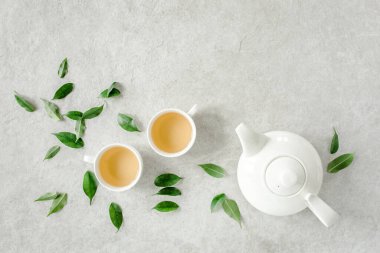 İki beyaz çay fincanı ve yeşil çay yapraklı çaydanlık ile bitki çayı. Düz yerde, üst tarafta. Çay konsepti