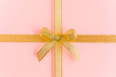 Pembe arka planda izole edilmiş, fiyonklu altın kurdele. Renkli bir kutlama, doğum günü geçmişi. Düz yatış, üst görünüm