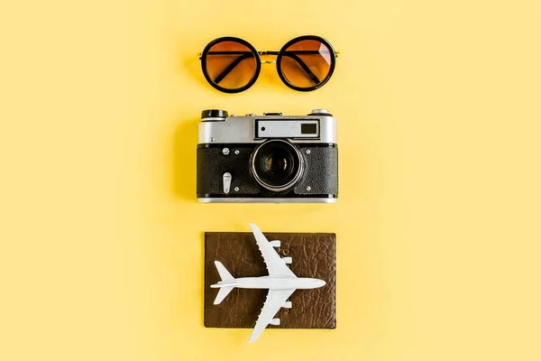 Conceito de acessórios para viajantes em fundo amarelo. Câmera retrô, avião modelo, avião e folha de palma tropical. — Fotografia de Stock