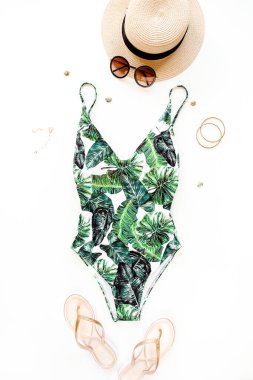 Kadın plaj aksesuarları: tropikal desenli mayo, beyaz arka planda hasır şapka. Yaz arkaplanı. 